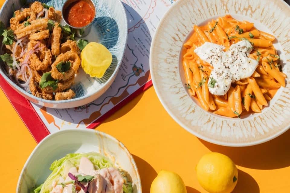 Colorful plates of fried calamari, sweet potato fries, and salad on yellow surface