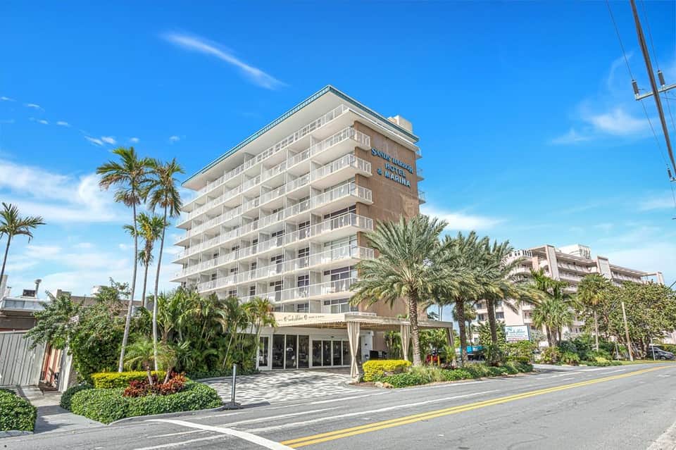 Beachfront hotel building exterior with palm trees, ground-level entrance, and clear blue sky