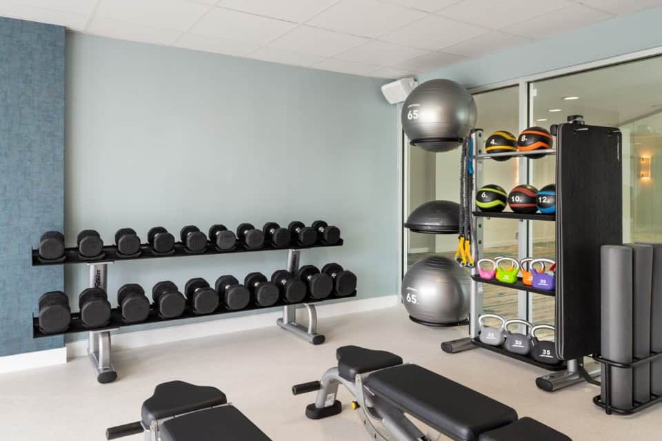 Hotel fitness center with dumbbell racks, medicine balls, exercise equipment, and mirrored walls