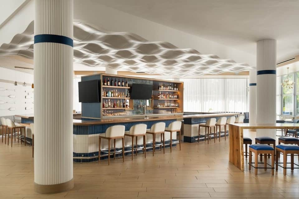 Contemporary hotel bar with cream-colored seating, textured ceiling, illuminated shelving, and fluted columns
