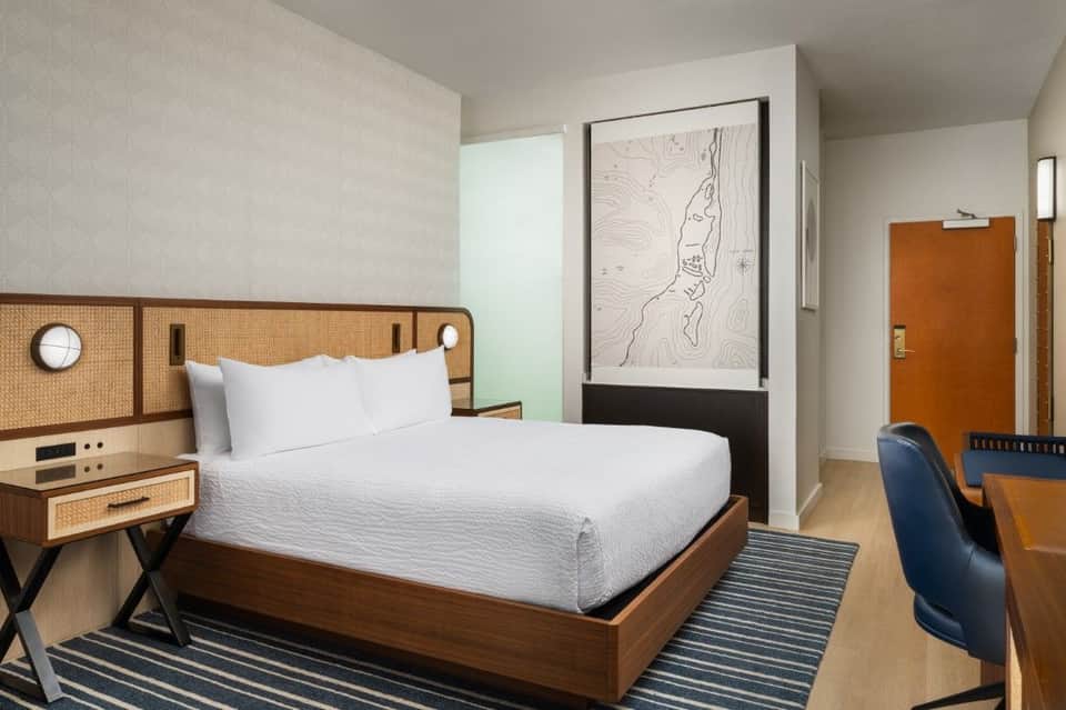 Modern hotel bedroom with woven headboard, white bedding, abstract art, and wood accents