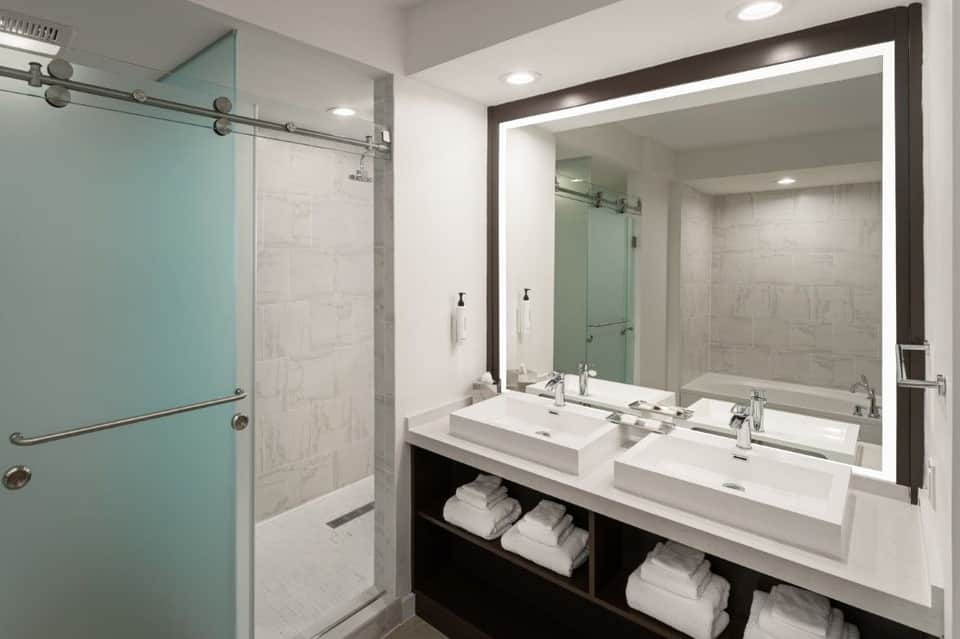 Luxury bathroom with dual vanity, turquoise glass shower door, large framed mirror, and white tile finishes