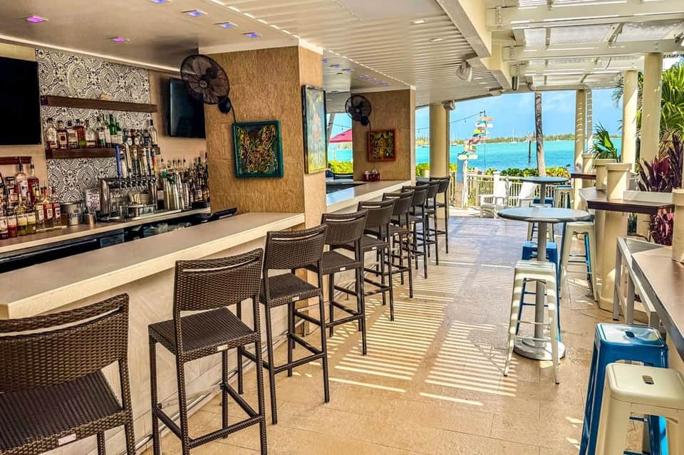Beachfront bar with woven chairs, ocean view, decorative wall art, and tropical plants