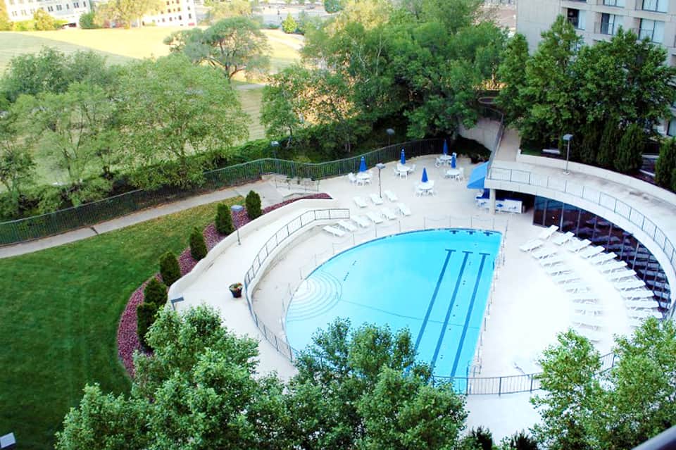 Aerial view of curved olympic-sized swimming pool surrounded by white lounge chairs and lush landscaping