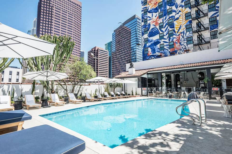 Resort pool deck with lounge chairs, umbrellas, and city skyline backdrop during daytime
