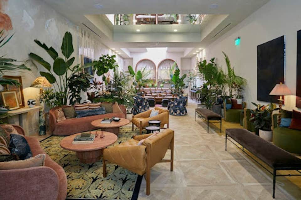 Luxurious hotel lobby lounge with terracotta seating, abundant potted plants, wooden tables, skylight, and arched doorways