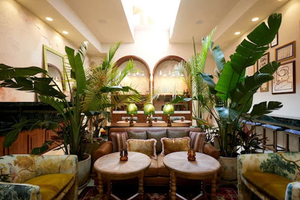 Upscale lounge with arched mirrors, tropical plants, and cream-colored furnishings