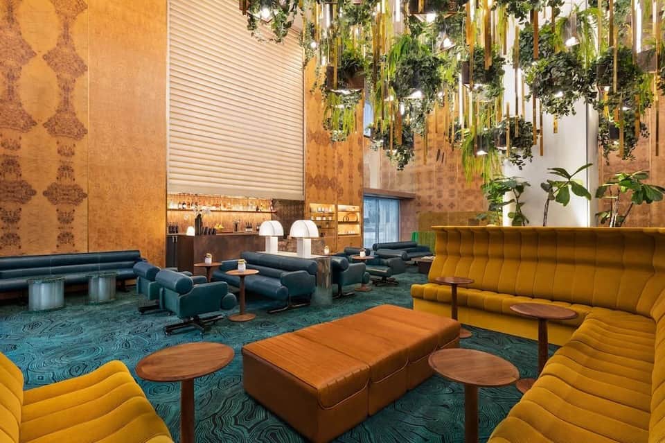 Modern hotel lobby lounge with colorful sectional seating, hanging plants, and gold-patterned walls