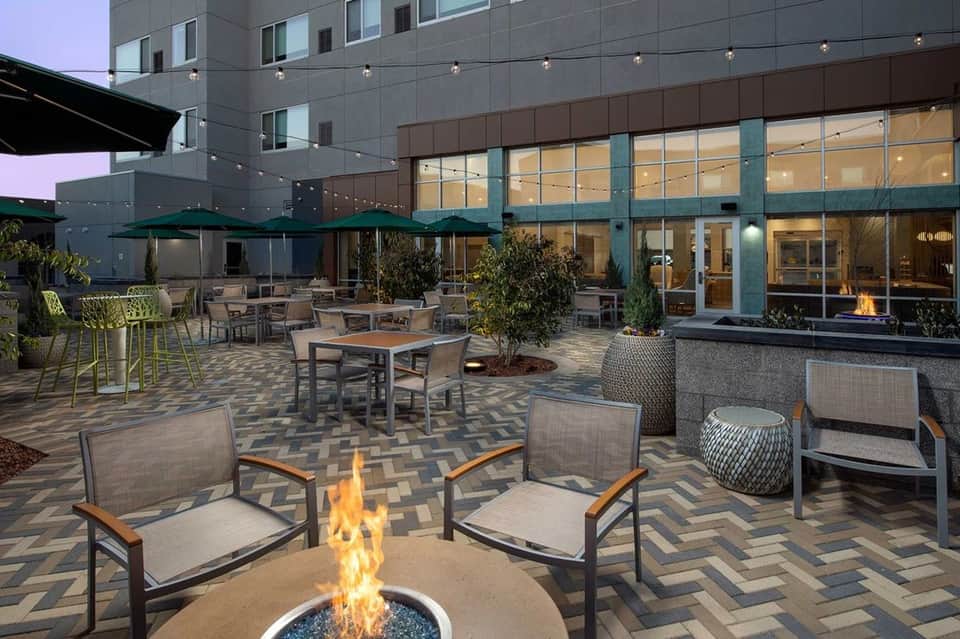 Evening courtyard with fire pit, lounge seating, green umbrellas, and modern hotel building facade