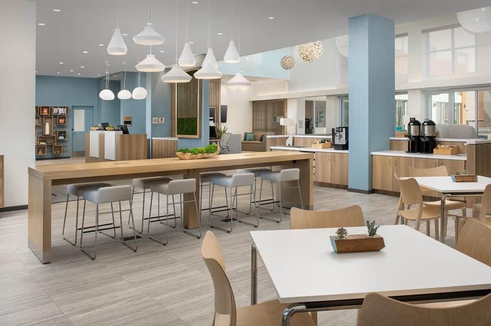 Modern hotel lobby with wooden bar counter, pendant lights, blue accent walls, and contemporary furnishings