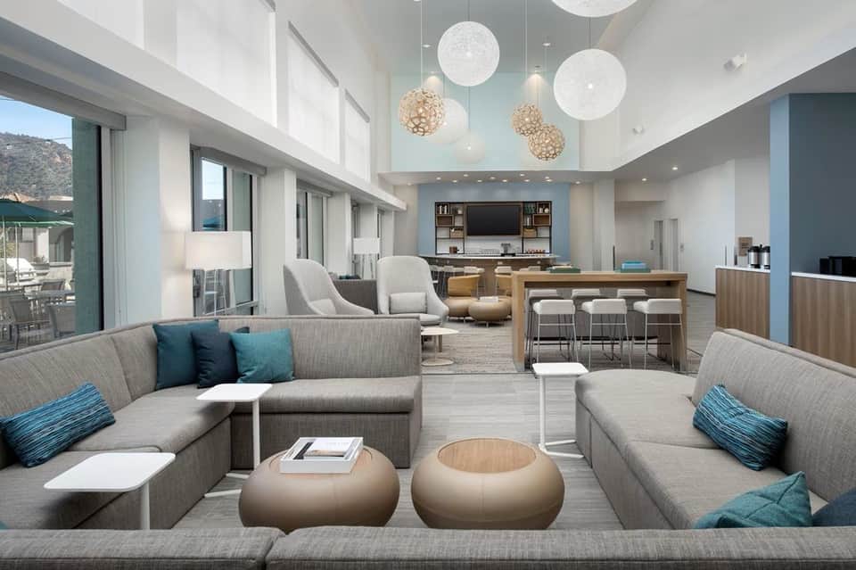 Open-concept lounge with L-shaped seating, hanging lights, bar area, and floor-to-ceiling windows