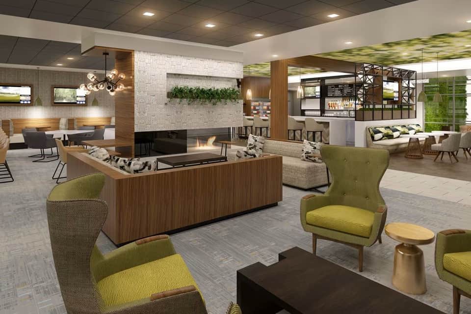 Modern hotel lobby with green accent chairs, pool table, fireplace, and bar area with contemporary wood and stone finishes