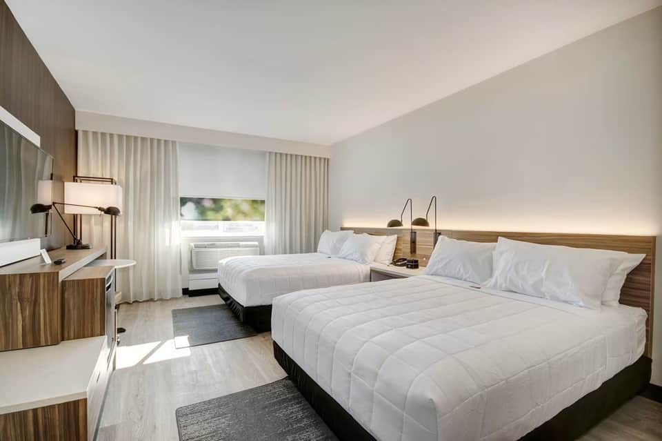 Double queen hotel room with two beds, wooden accents, desk area, and ambient lighting