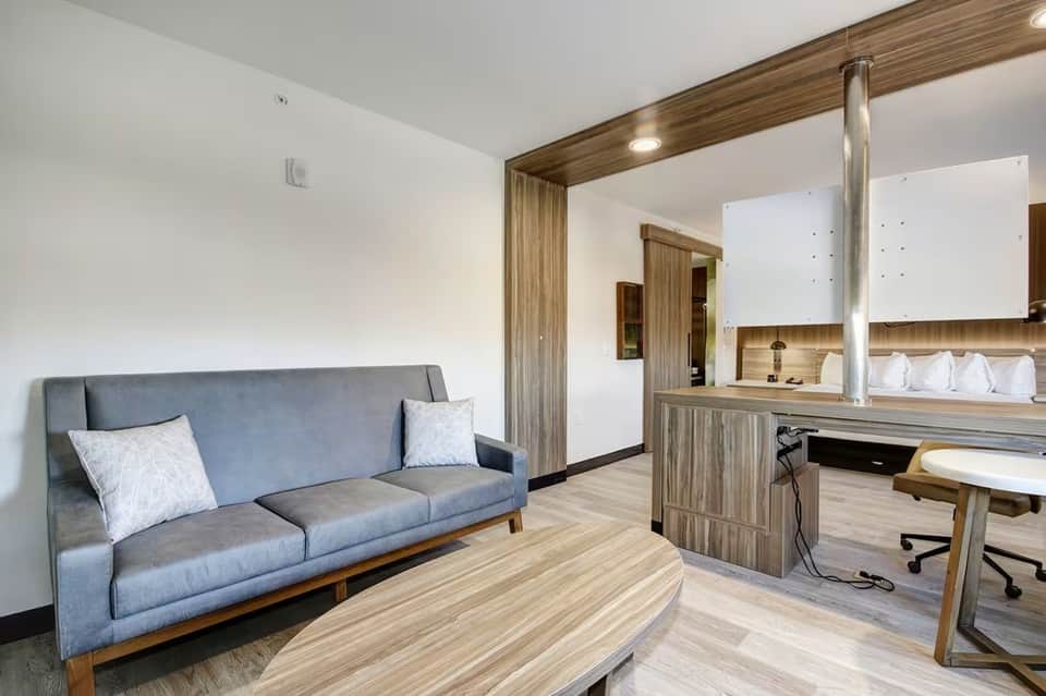 Hotel suite living area with gray sofa, wooden desk, workspace, and modern furnishings