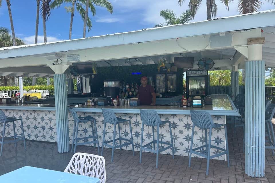 Beachfront bar counter with blue patterned stools, palm trees, and covered serving area at tropical resort