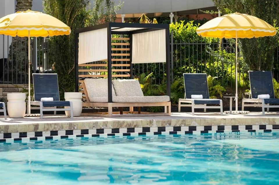 Resort pool with lounge chairs, yellow umbrellas, and modern pergola with lush green landscaping