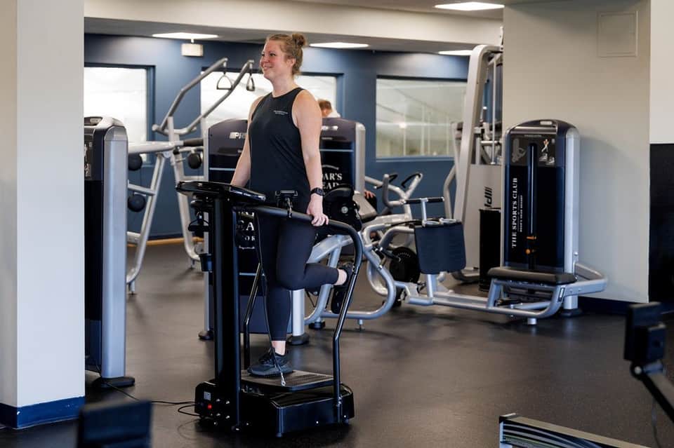 Gym interior with woman on stationary bike, surrounded by cardio and strength training equipment
