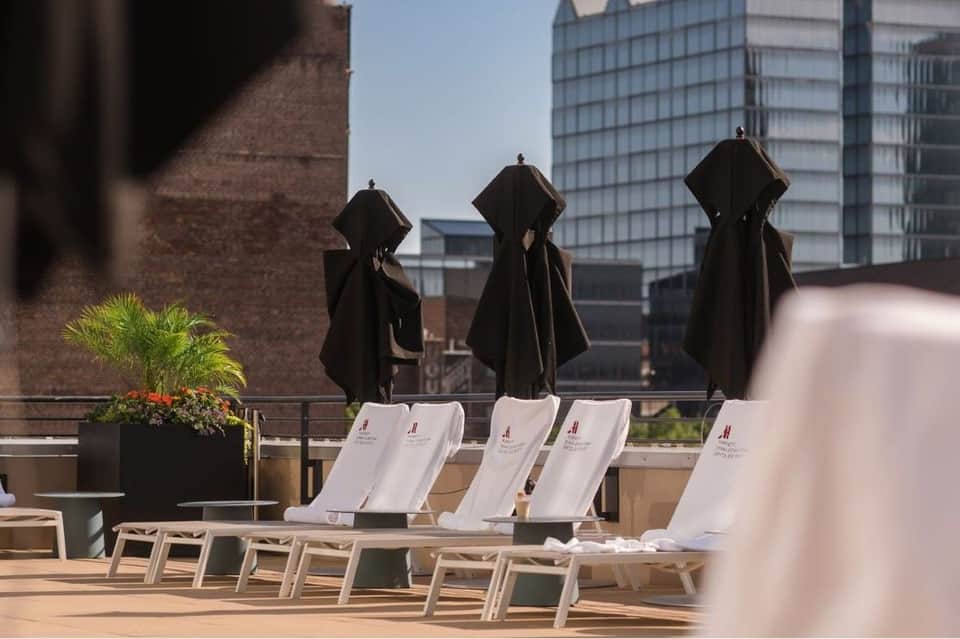 Rooftop terrace with white lounge chairs, black umbrellas, and city skyline views with brick buildings