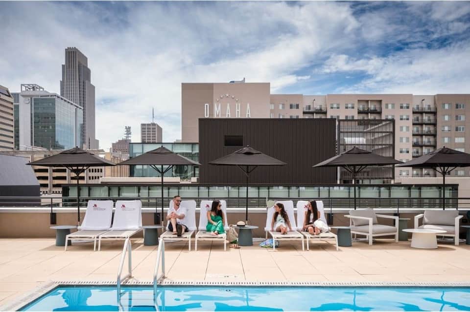 Rooftop pool deck with lounge chairs and umbrellas overlooking Omaha skyline during daytime
