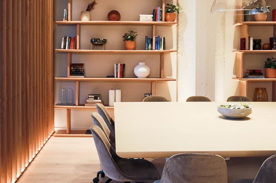 Modern office interior with white desk, wooden shelving unit filled with books and plants, and contemporary seating