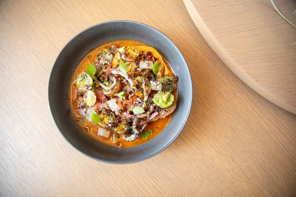 Gourmet dish with meat, vegetables, and sauce in gray bowl on wooden table