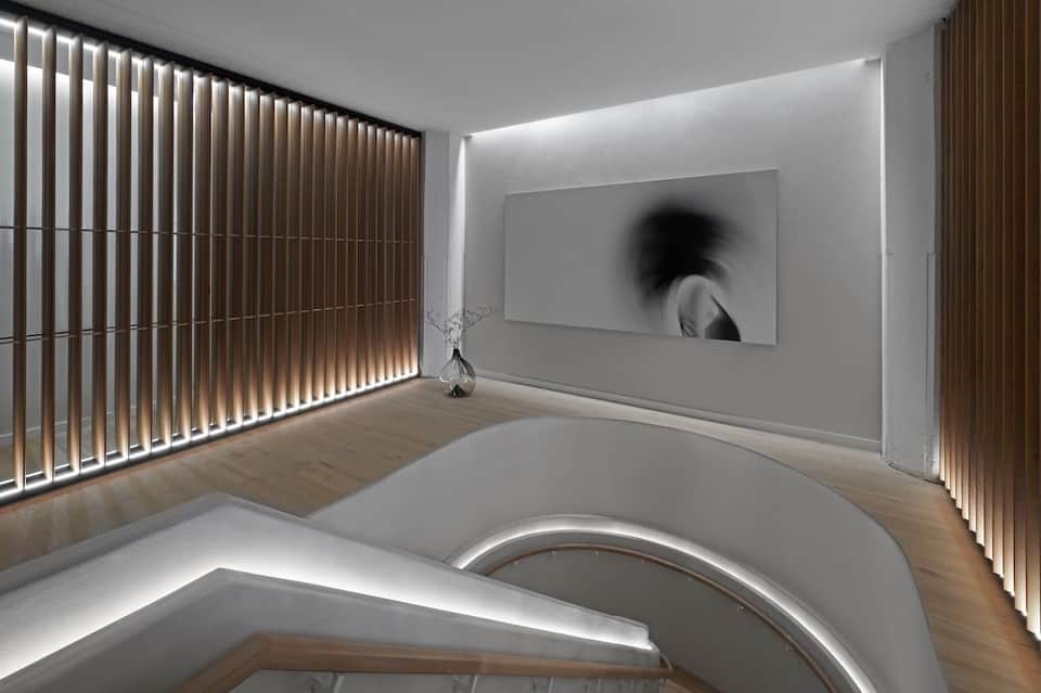 Modern minimalist gallery space with white walls, wooden flooring, and artistic display