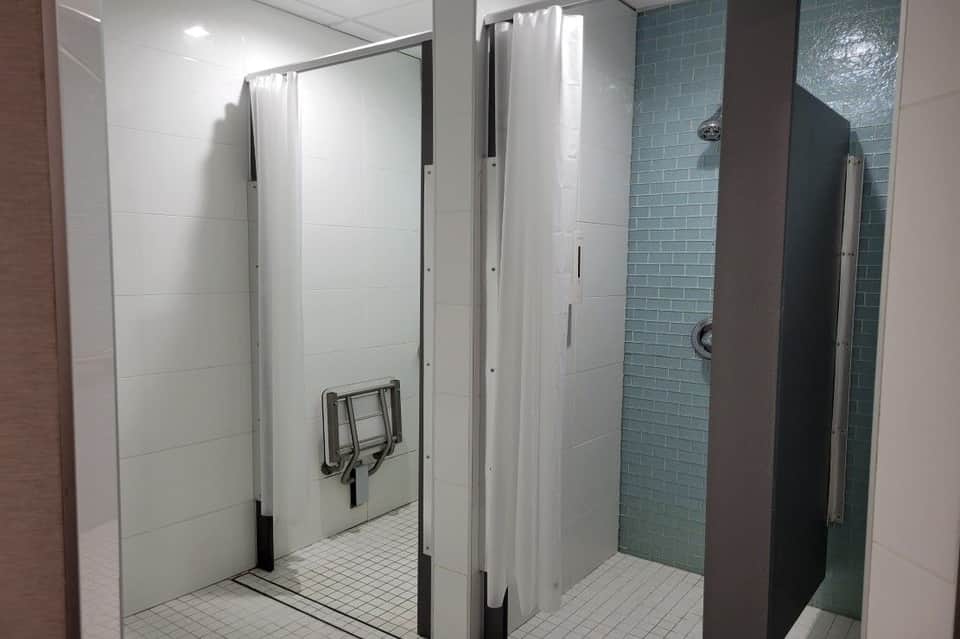 Public restroom with white tile walls, individual shower stalls with privacy curtains, and teal accent tile
