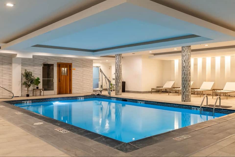 Indoor swimming pool with blue water, decorative columns, lounge chairs, and modern ceiling design