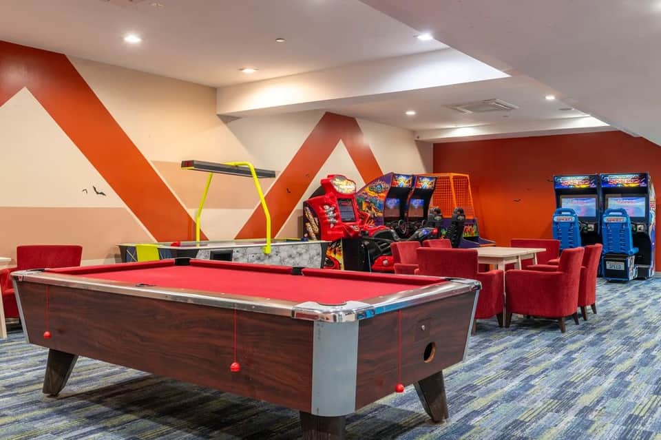 Game room with pool table, arcade games, red accent chairs, and modern geometric wall art