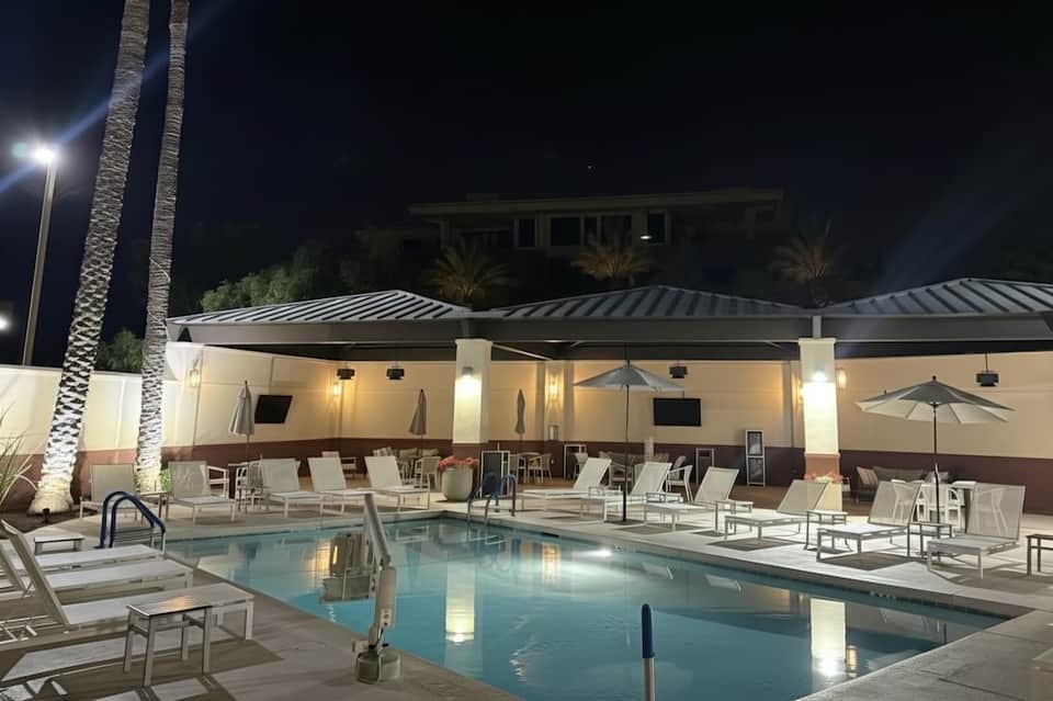 Nighttime pool area with illuminated cabana and lounge chairs under palm trees