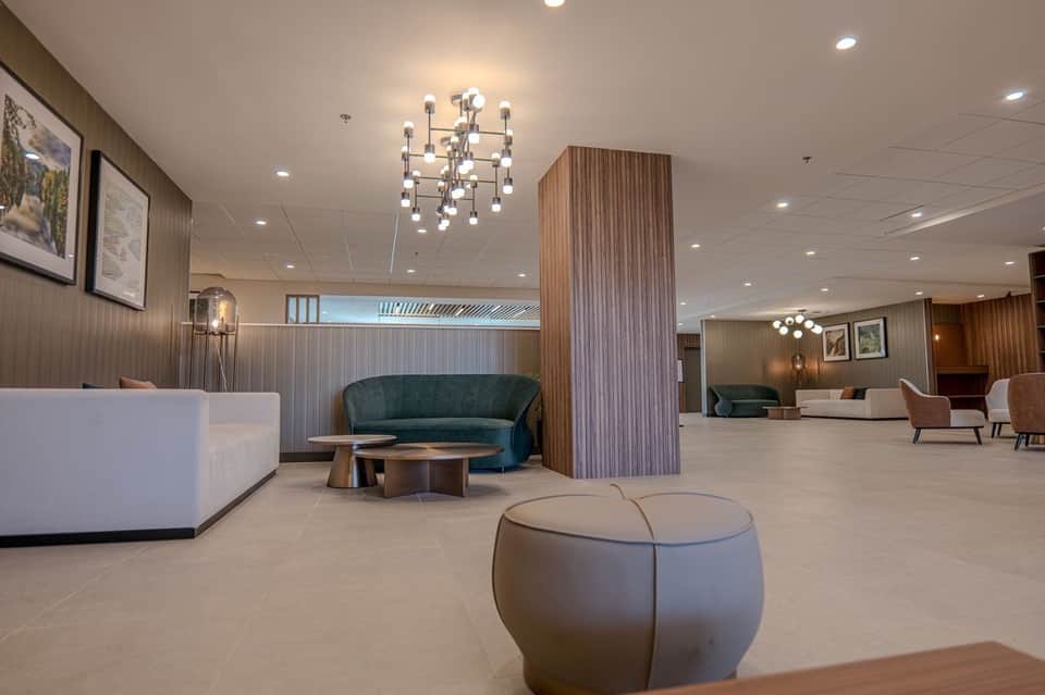 Modern hotel lobby with white reception desk, teal curved sofa, wood accent wall, and contemporary lighting