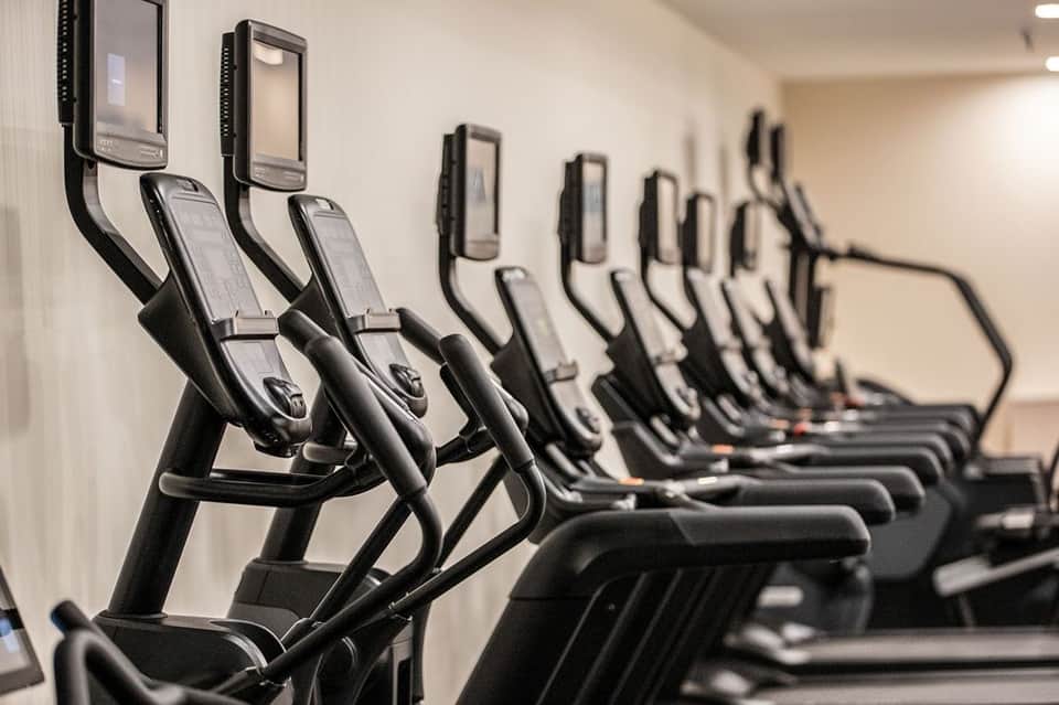 Row of elliptical machines with digital displays lined against a white wall in a gym