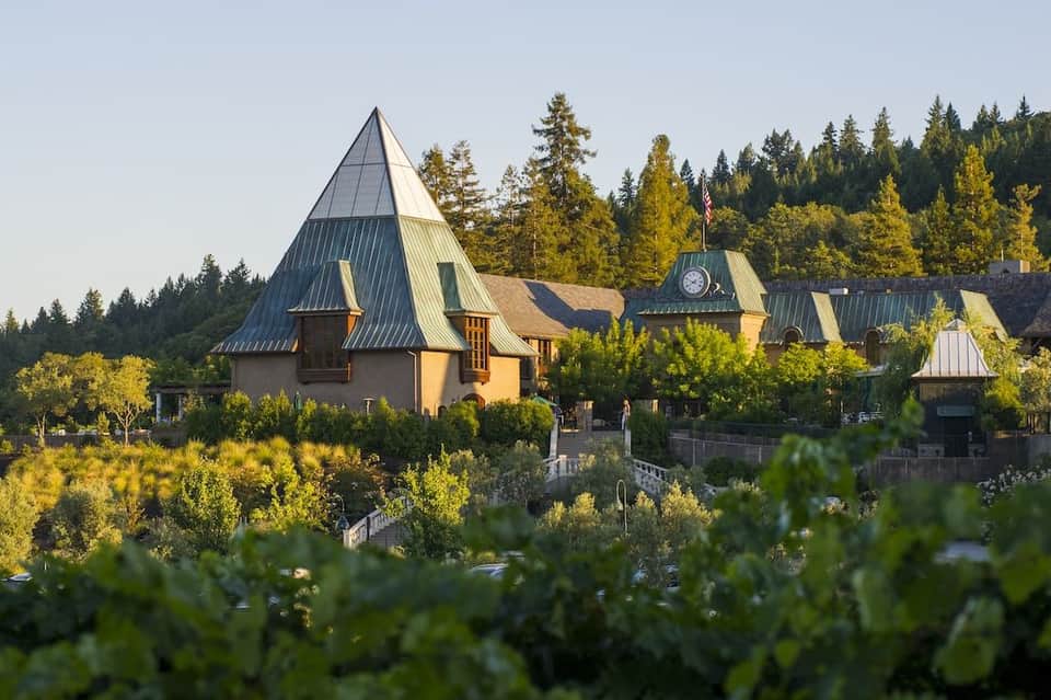 Castle-like winery building with distinctive pointed turrets and metal roofs nestled in forested vineyard