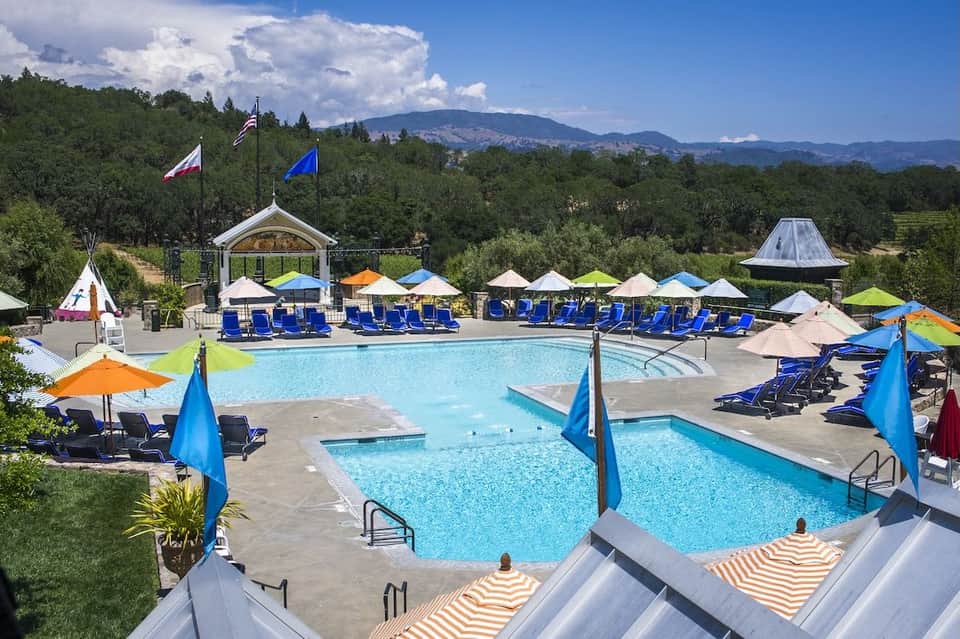 Resort pool area with multiple pools, blue loungers, colorful umbrellas, and mountain views in background
