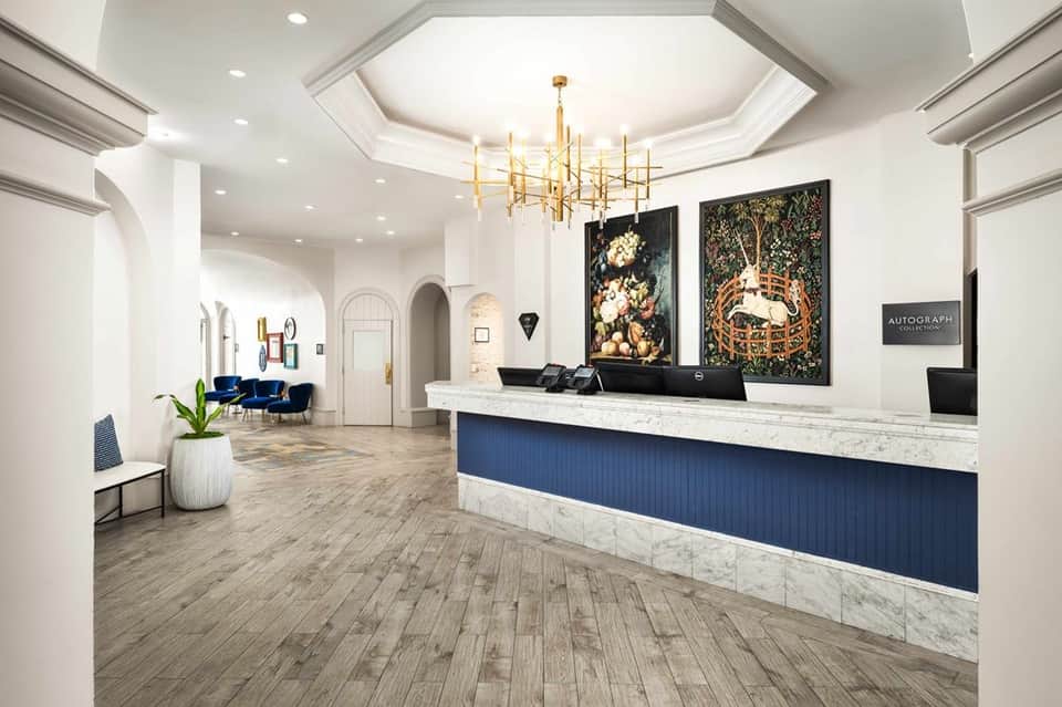 Modern hotel lobby with marble reception desk, gold chandelier, and blue velvet seating area