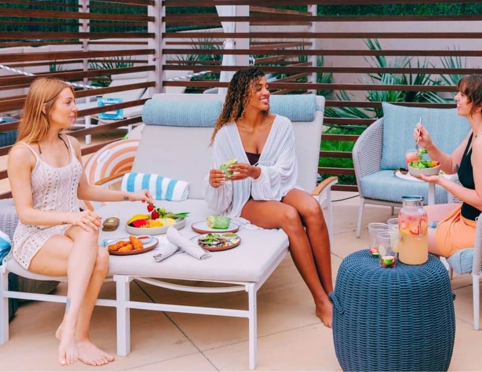 Three women enjoying lunch on modern beachside deck with striped lounge chairs