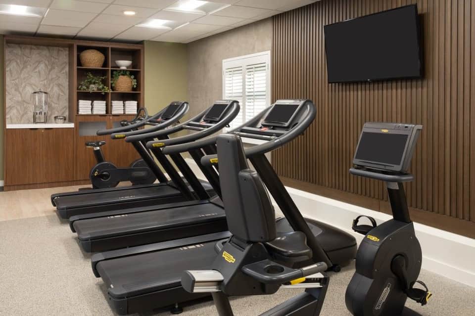 Modern hotel fitness center with treadmills, stationary bikes, and exercise equipment against wood-paneled walls