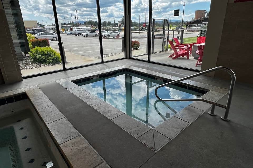 Indoor lap pool with concrete deck, metal handrails, and red chairs beside large windows