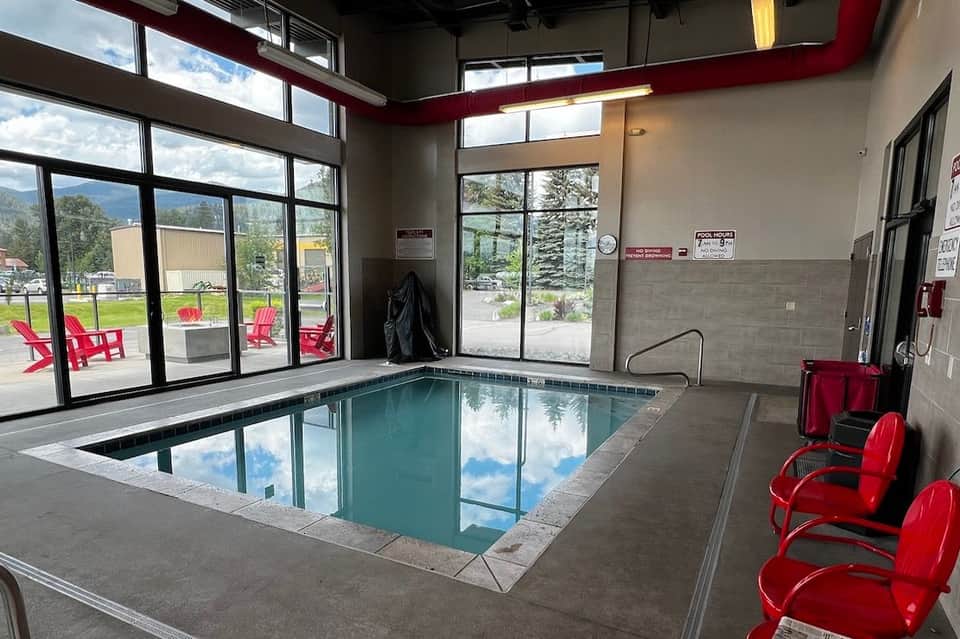 Indoor heated pool with rectangular lap lanes, windows overlooking outdoor patio with red chairs