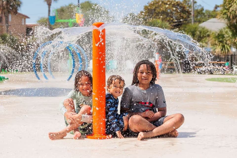 Children playing in interactive water splash pad with orange center column and spraying water