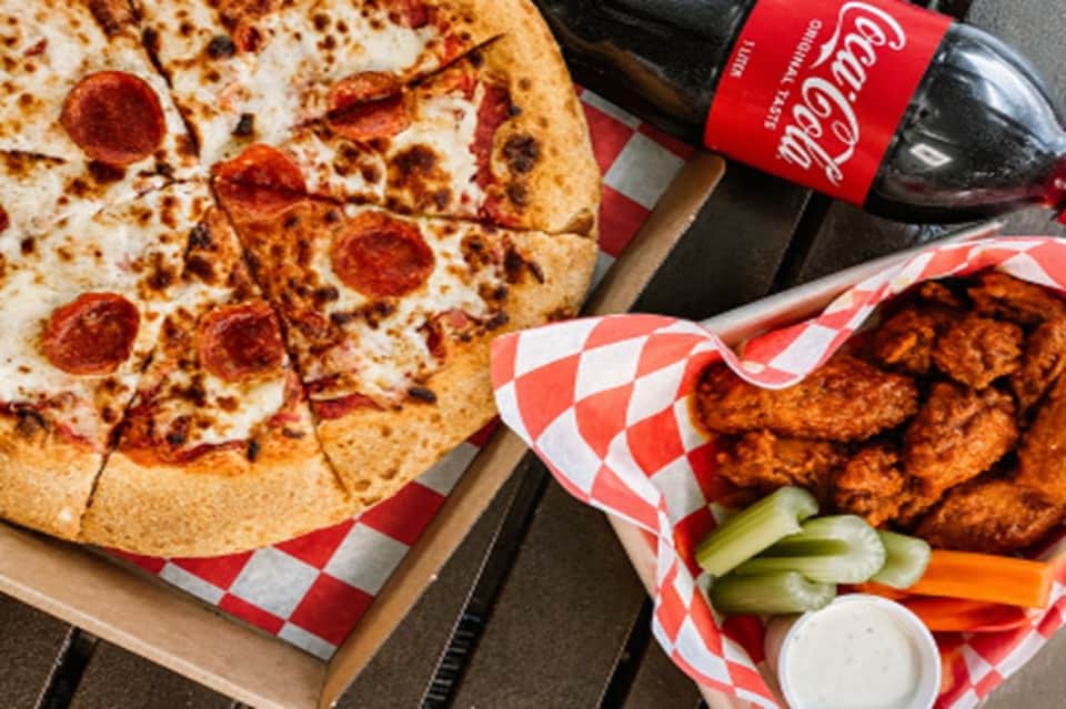 Pepperoni pizza and fried chicken wings with beverage on red checkered paper