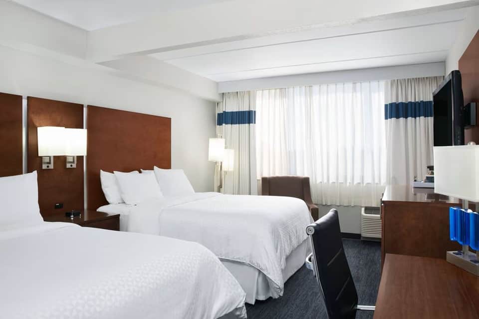 Hotel guest room with two queen beds, brown headboards, and city windows