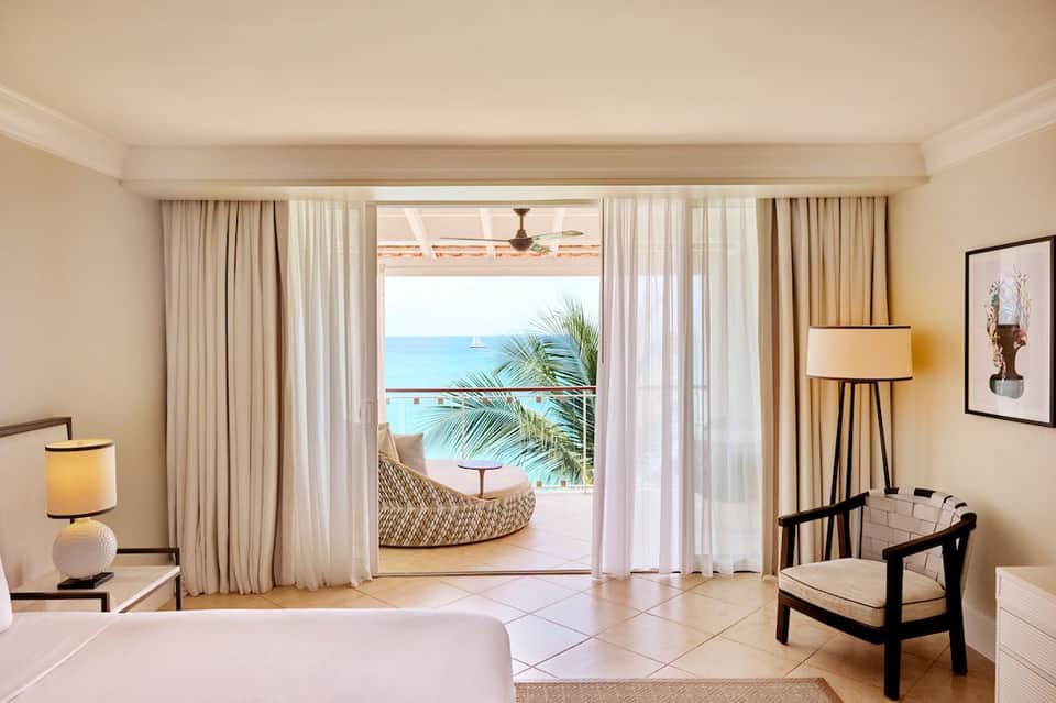 Luxury beachfront hotel room with ocean view terrace, elegant furnishings, and direct access to white sand beach