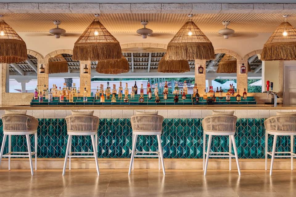 Modern beachfront bar with woven lampshades, teal tile backsplash, wooden barstools, and ocean view
