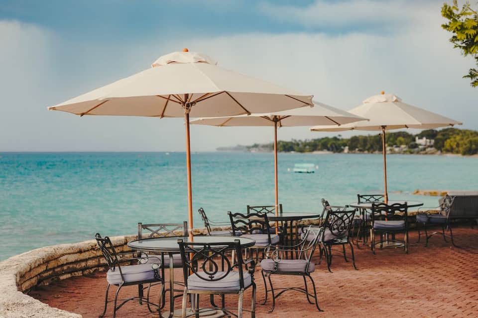 Beachside dining area with cream umbrellas, metal chairs, and turquoise water views