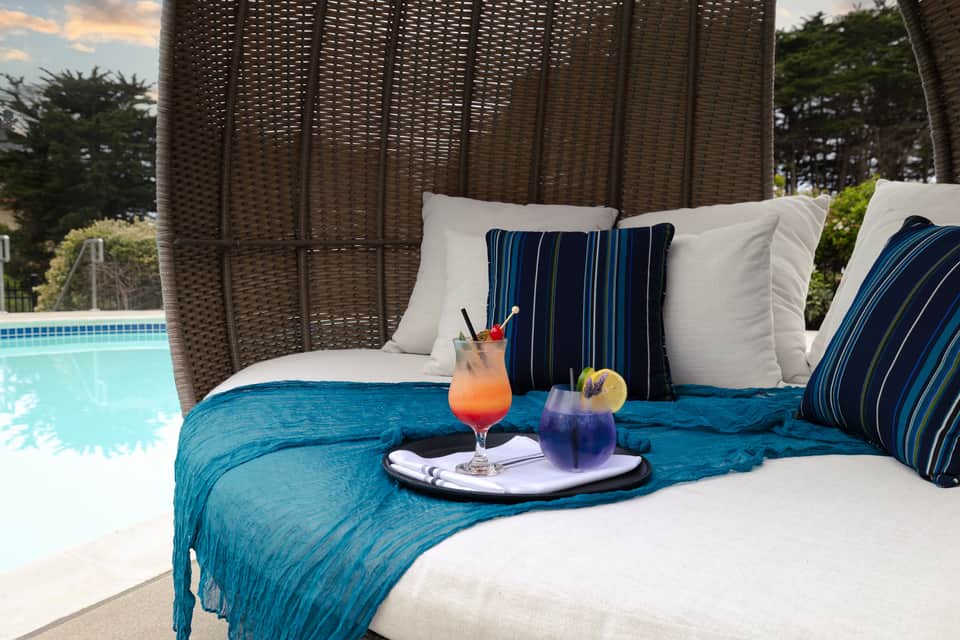 Wicker pod lounge chair by pool with blue cushions, cocktails, and ocean view
