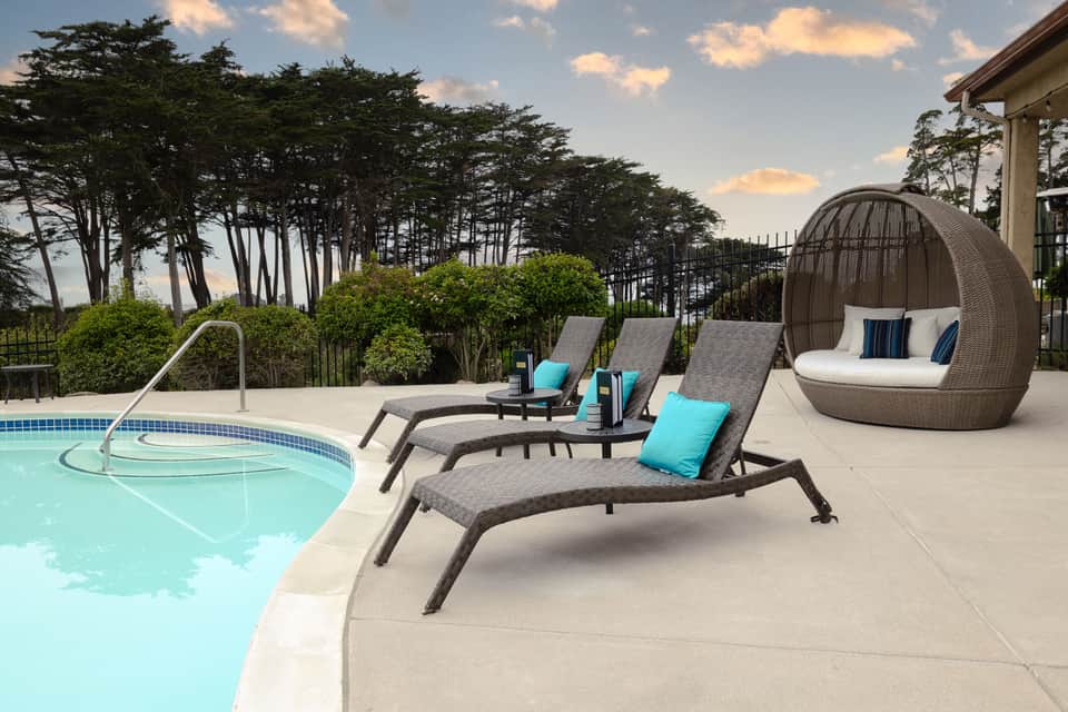 Curved pool edge with three chaise lounges and woven sphere chair overlooking landscaped grounds at sunset
