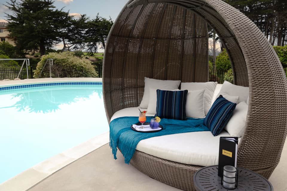 Interior view of large woven egg chair with white bedding, turquoise throw, and striped pillows by pool