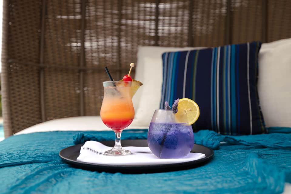 Colorful cocktails on tray inside woven egg chair with striped pillows and white bedding