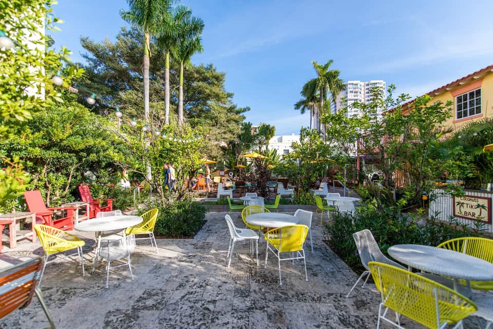 Colorful courtyard with yellow and green chairs, tables, tropical vegetation, and resort buildings